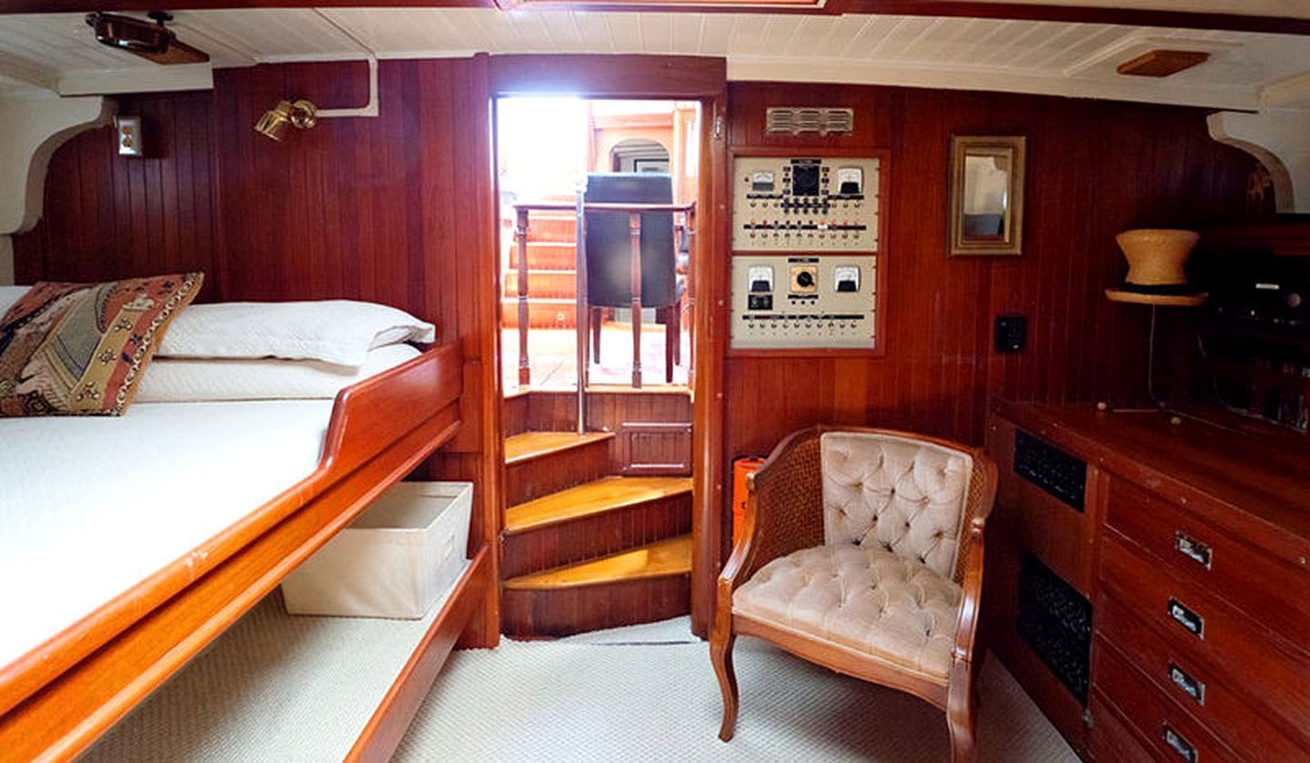 Una cabaña de madera con una cama, una silla, una escalera y un panel de control.