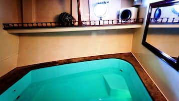 Un hidromasaje pequeño y rectangular con un borde marrón, un estante encima con un adorno, y un espejo fijado a la pared.