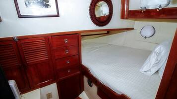 Una cabaña acogedora con una cama alta, un pequeño aparador de madera con cajones, un espejo y un cuadro en la pared.