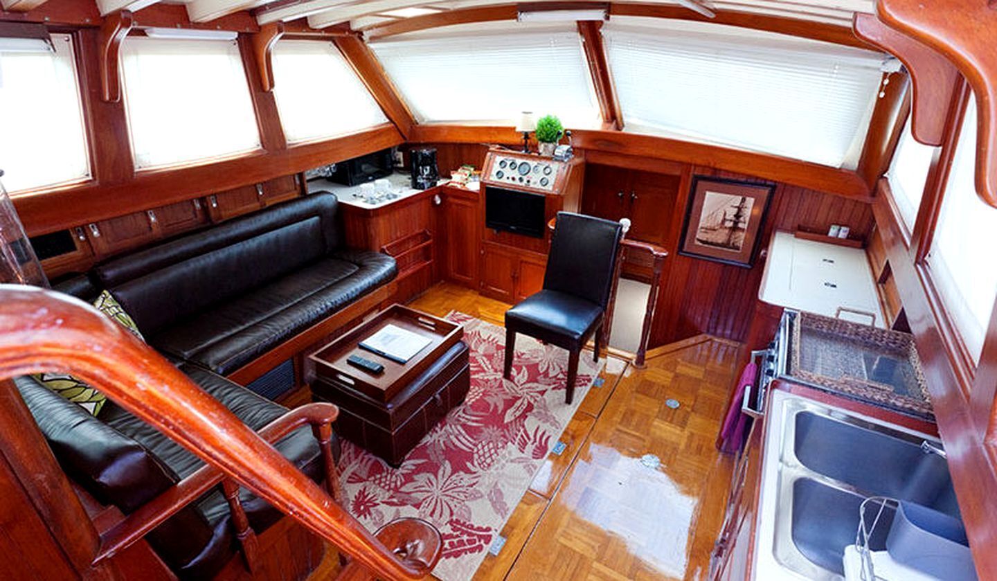 Un espacio interior compacto con sofá, una mesita, una silla, un panel de control y una ventana.