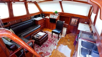 Un espacio interior compacto con sofá, una mesita, una silla, un panel de control y una ventana.