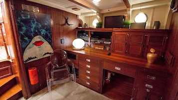 Una cocina pequeña con armarios de madera, una silla transparente, un cuadro y un televisor.