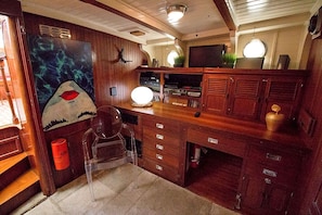 A compact kitchen with wooden cabinets, a clear chair, a painting, and a television.