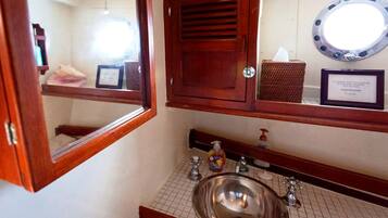 Un baño con tocador de madera, un lavamanos, un espejo y un certificado enmarcado en la pared.