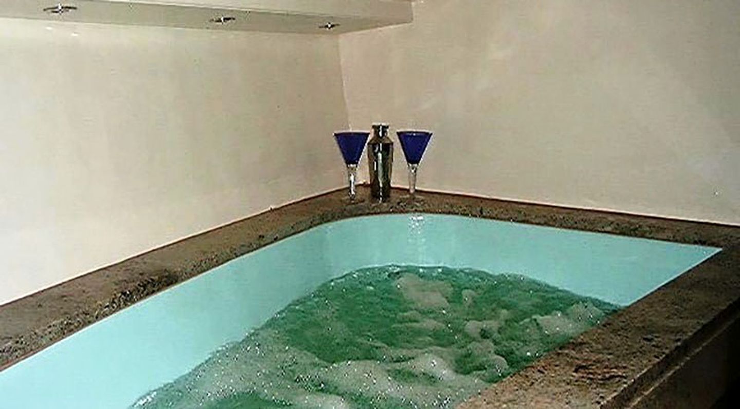 Una piscina rectangular con agua cristalina, dos grifos azules y suelo de baldosas.