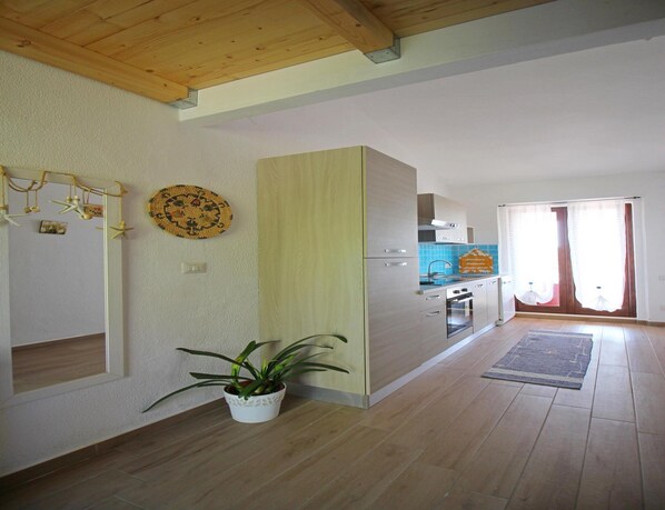 A modern kitchen with wooden cabinets, a built-in oven, and a sink. There is a potted plant on the floor and a decorative wall hanging. - Apartment in Costa Rei Near White Sand Beaches (Muravera)