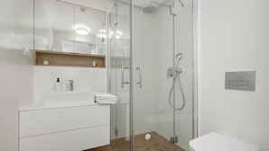 Une salle de bain moderne avec une douche à parois de verre, des toilettes blanches et un meuble-lavabo avec un miroir et des rangements.