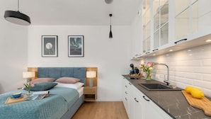A compact room with a bed, bedside table, lamp, and a kitchenette with a sink and countertop. - Holiday Studio Near the Beach, Pool, Sauna (Rewal)