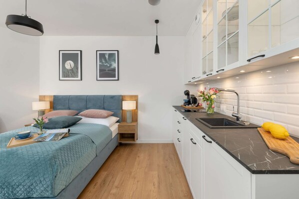 A compact room with a bed, bedside table, lamp, and a kitchenette with a sink and countertop. - Holiday Studio Near the Beach, Pool, Sauna (Rewal)