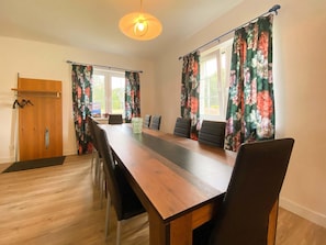 Ein Konferenzraum mit einem langen Holztisch, vier Stühlen, einer Holztür und floralen Vorhängen.