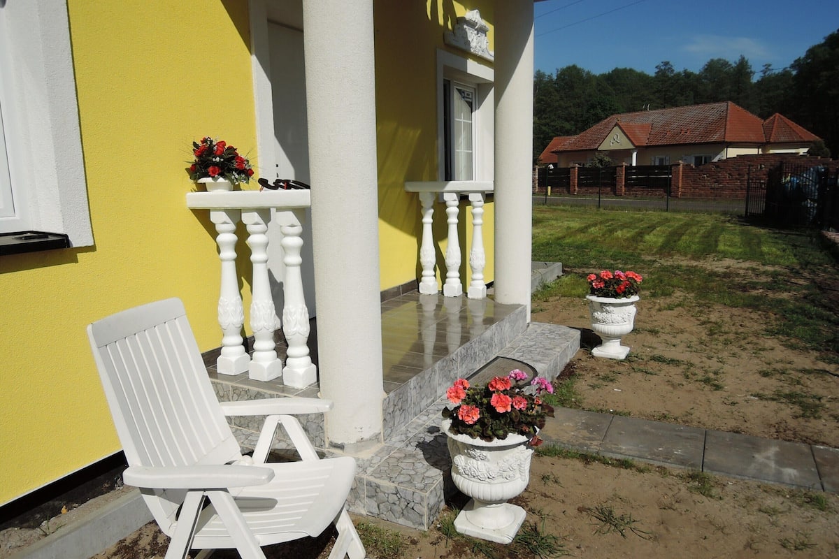 A yellow building with a white porch, white balustrades, and potted flowers.