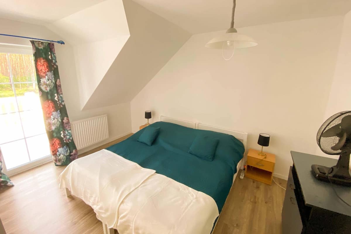 A bedroom with a bed, a ceiling fan, a radiator, and a window with curtains.