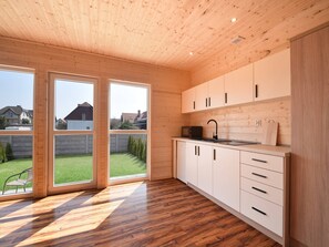 A modern kitchen with wooden cabinets, a black faucet, and a large window overlooking a backyard. - Comfortable, Single-story Holiday Homes (gmina Sianów)