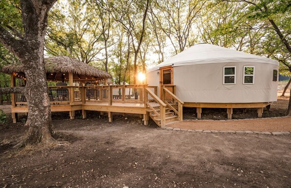 A yurt with a wooden deck, a thatched roof structure, and a white exterior.