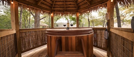 A wooden gazebo with a round table and chairs, surrounded by bamboo fencing and trees.