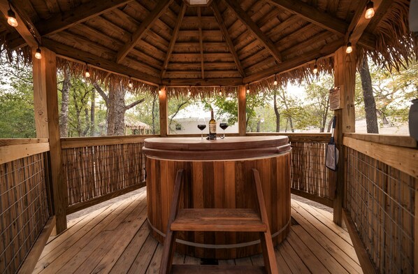 A wooden gazebo with a round table and chairs, surrounded by bamboo fencing and trees.