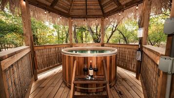 A wooden hot tub with a wooden deck, surrounded by a bamboo fence, and a wooden pergola overhead.