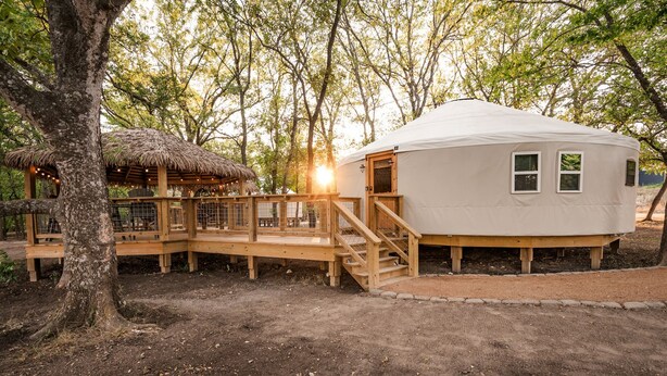 A yurt with a wooden deck, a thatched roof structure, and a white exterior. - A Yurt for Everyone: Family and Friends Getaway in Bandera, TX (Bandera)