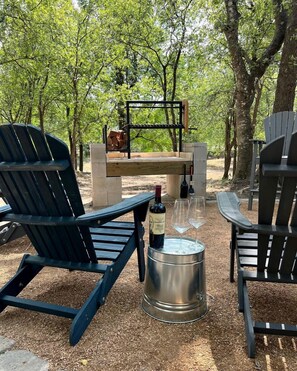 An outdoor seating area with Adirondack chairs, a metal barrel, and a bottle of wine. - A Yurt for Everyone: Family and Friends Getaway in Bandera, TX (Bandera)
