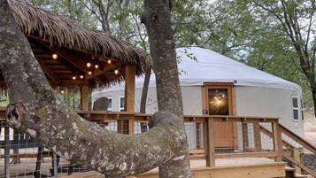 A treehouse with a thatched roof and wooden deck, connected to a cabin with a white exterior.