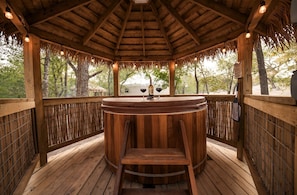 Un gazebo in legno con un tavolo rotondo e sedie, circondato da staccionate di bambù e alberi.