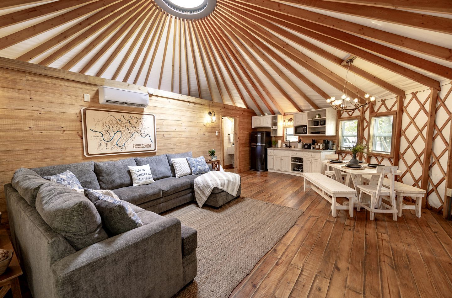 A spacious living area with a large sofa, a dining table with chairs, a kitchen area, and a wooden ceiling structure.