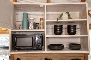 A kitchen with a GALAZ microwave, measuring cups, cooking spray, and black bowls on shelves.