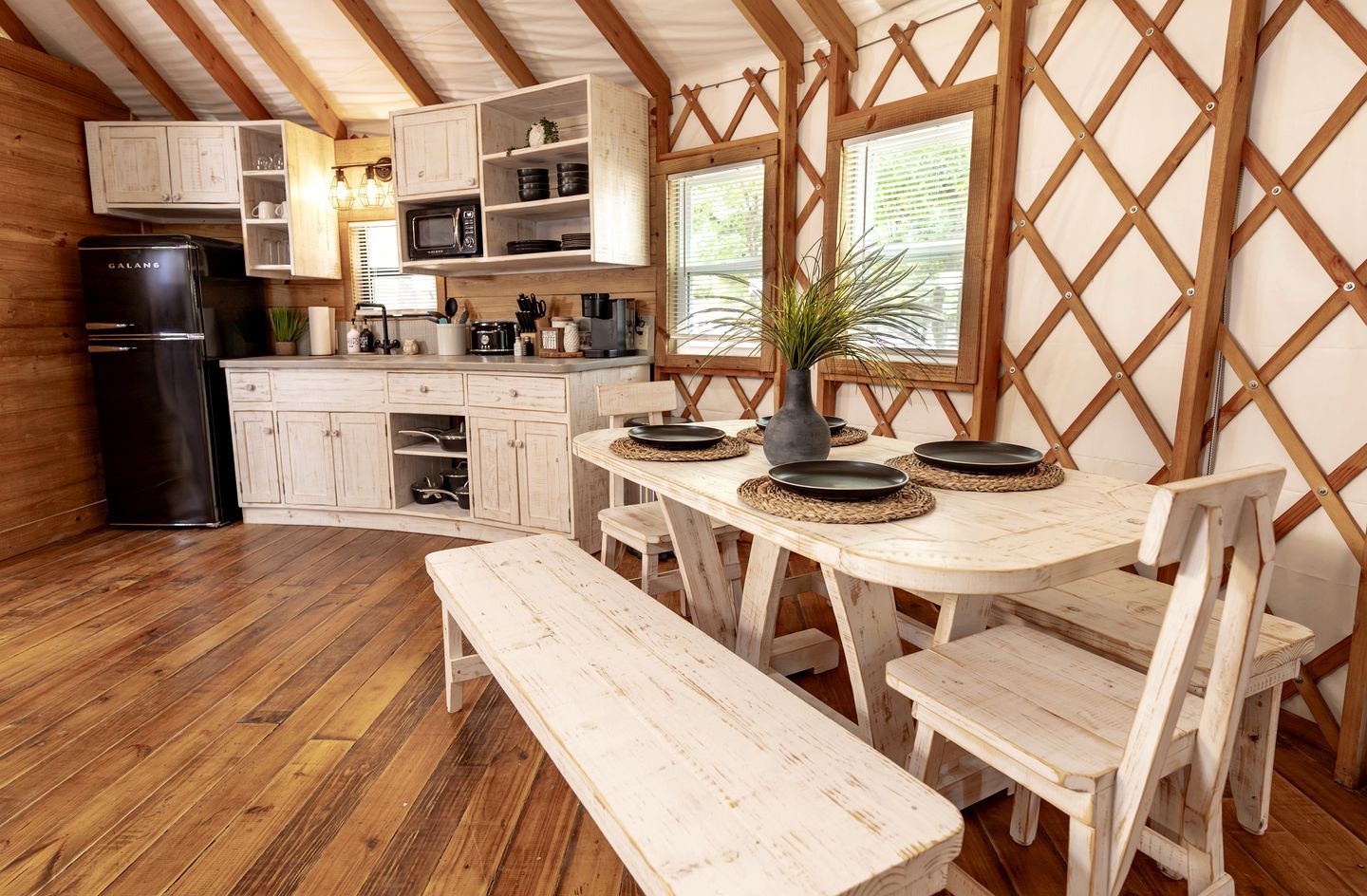 Une cuisine rustique avec des meubles de rangement en bois, un réfrigérateur noir et un coin repas comprenant un banc et des chaises.