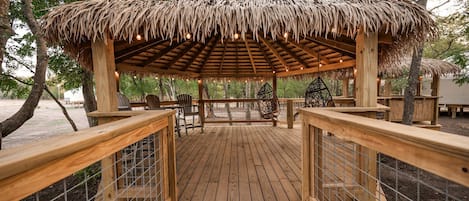Una terraza de madera con estructura de techo de paja, rodeada de árboles.