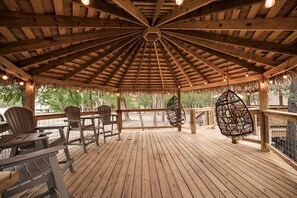 A wooden gazebo with a thatched roof, seating area, and hanging chairs.