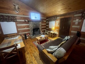 Ein gemütliches Blockhaus-Interieur mit Kamin aus Stein, Holzmöbeln und einem an der Wand befestigten Fernseher.