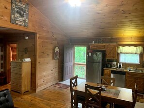 L’intérieur d’un chalet en bois comprend un coin repas, une cuisine et une porte donnant sur un balcon.