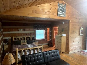 Ein Ferienhäuschen-Interieur mit einem Bett, einem Holzschrank, einem Fenster mit Vorhängen und einer an der Wand befestigten Uhr.