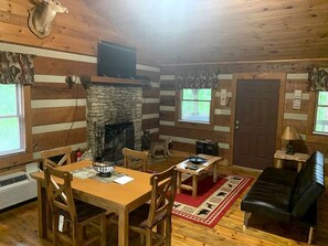 Ein rustikales Blockhaus-Interieur mit Kamin aus Stein, einem Holzespeisetisch und einer Ledersitzgruppe.