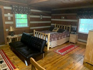 Une chambre de style rustique avec un lit, un canapé en cuir noir, un plancher en bois et une fenêtre avec des stores.