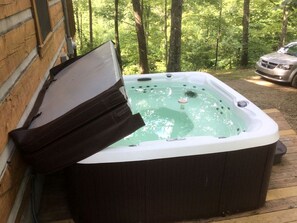 Ein Whirlpool neben einer Holzhütte mit Wald im Hintergrund.