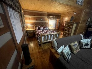 A cozy cabin-style room with a wooden bed, a small table, and a dresser. - Enchanting Log Cabin in the Woods just Outside of Gatlinburg, Tennessee (Sevierville)