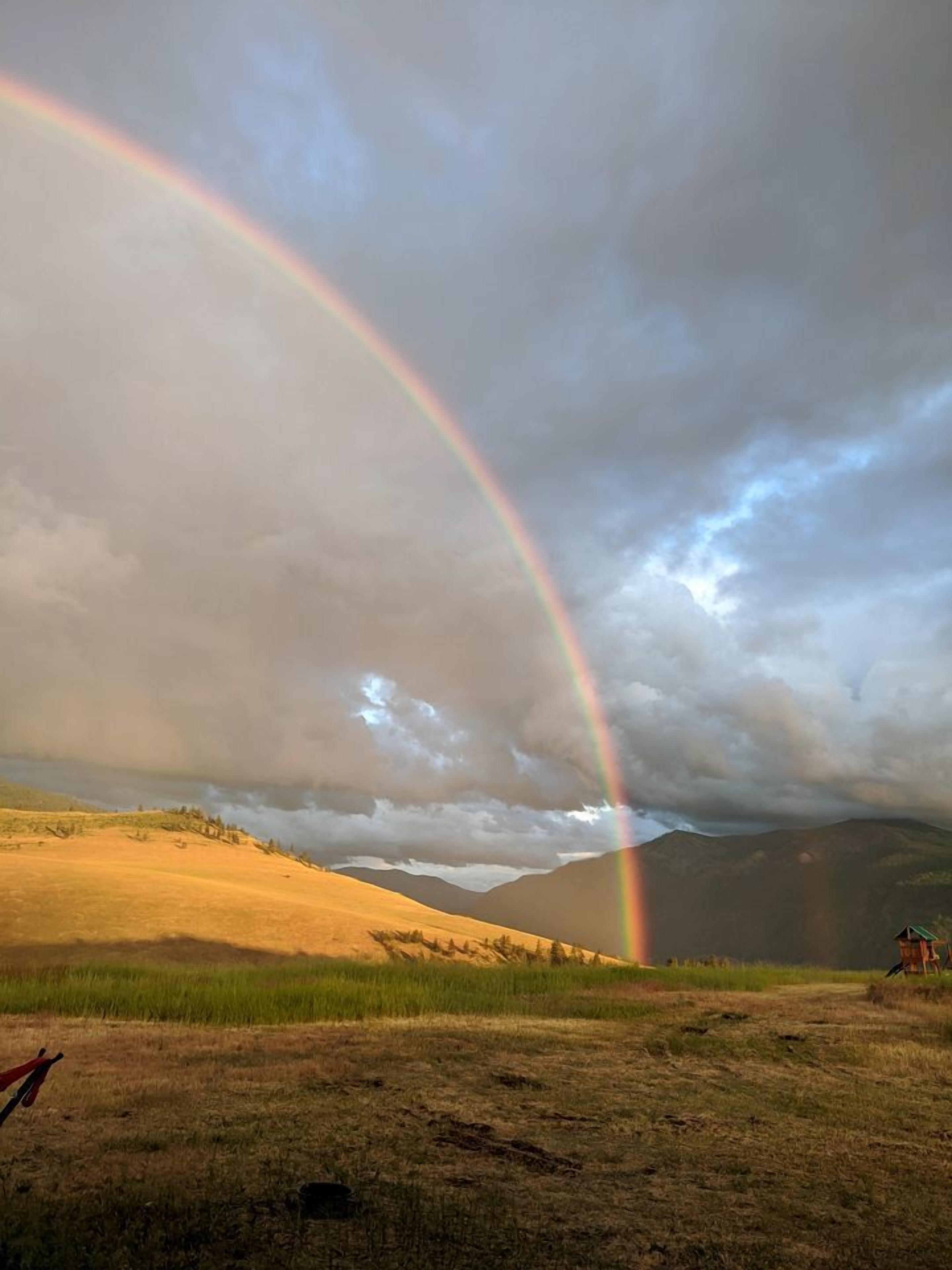 A landscape with a rainbow, grassy fields, and distant mountains.