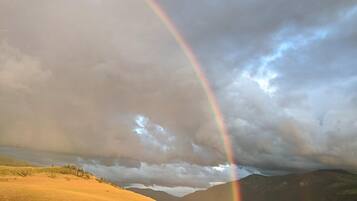 A landscape with a rainbow, grassy fields, and distant mountains.