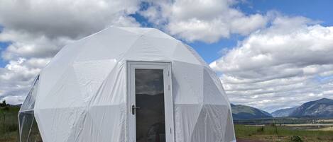 A dome-shaped tent with a door and a window, set on a wooden platform with a landscape view in the background.