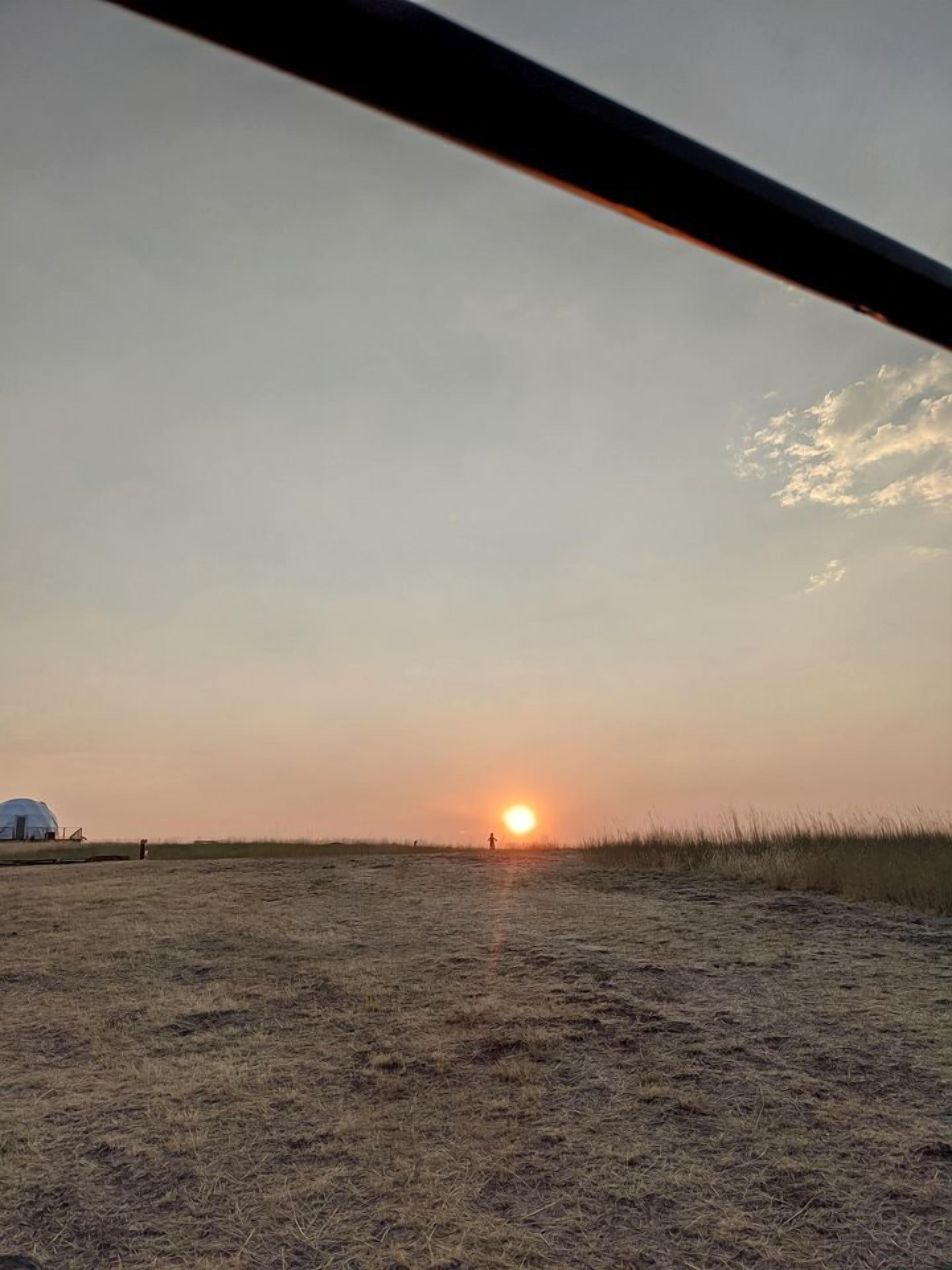 A sunset over a grassy field with a dome structure in the distance.