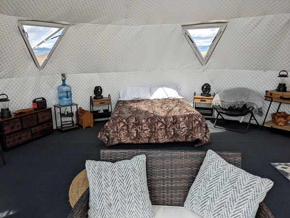 A tented room with a bed, two windows, a water dispenser, a radio, and a lantern.