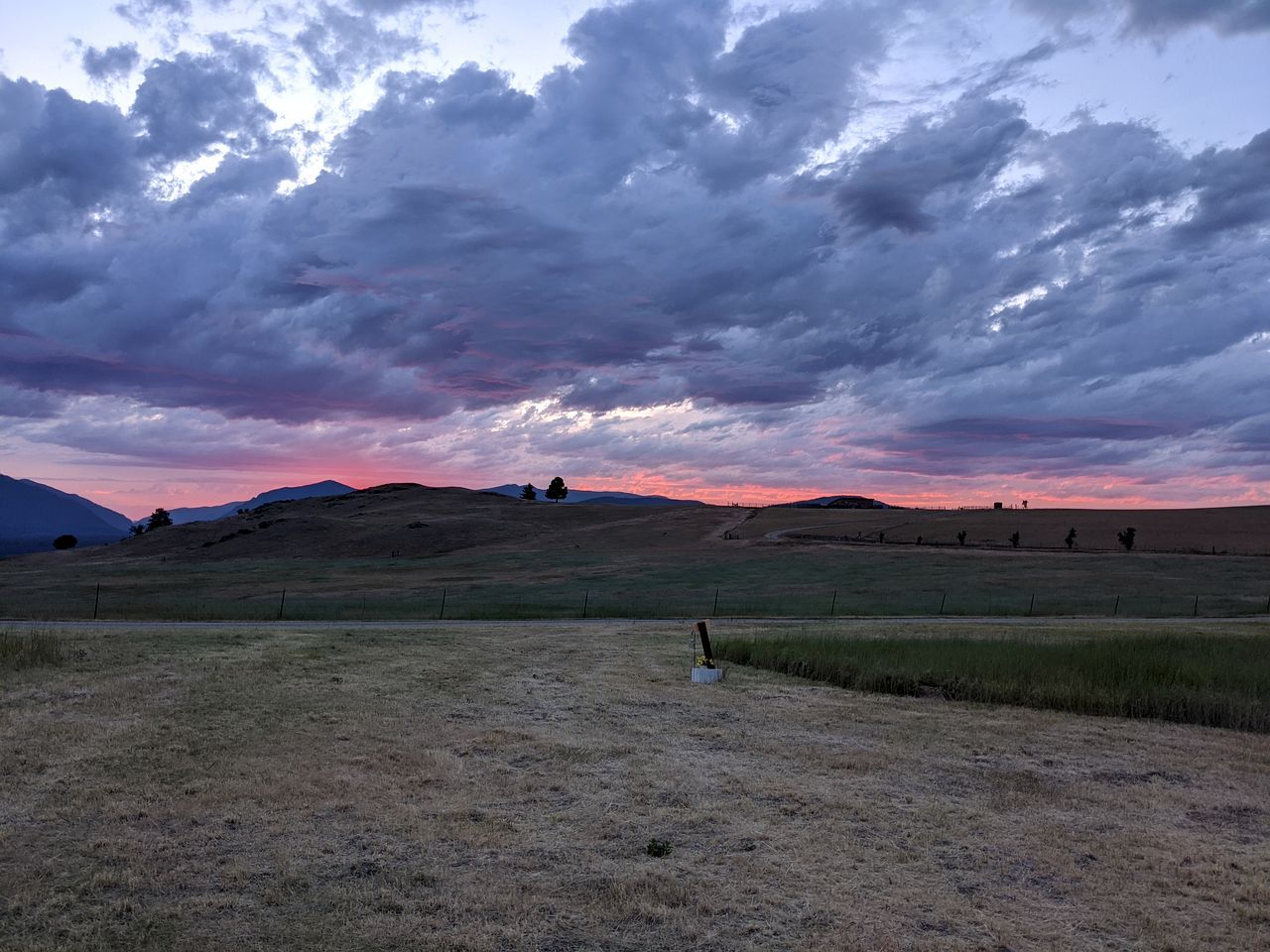 A rural landscape with rolling hills, a fence, and a distant tree line.