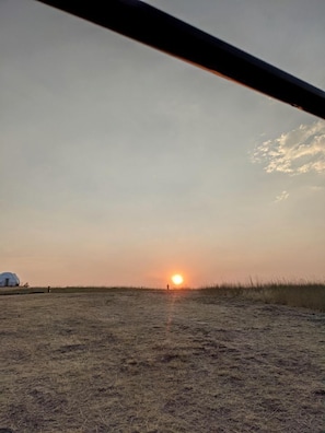 Un coucher de soleil sur un champ herbeux, avec une structure en forme de dôme visible au loin.