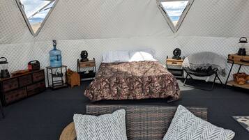 A tented room with a bed, two windows, a water dispenser, a radio, and a lantern.