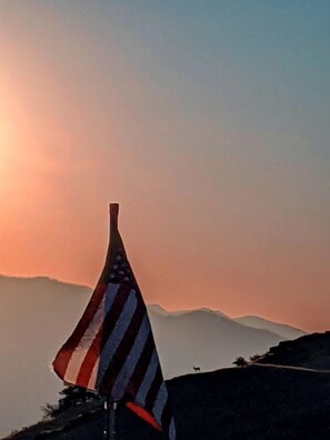 A flagpole with an American flag, set against a backdrop of mountains and a sunset sky.