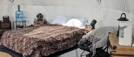 A cozy room with a bed, a small table, a chair, a water dispenser, and a fan.