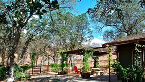 A covered outdoor seating area with tables and chairs, surrounded by potted plants and trees. - Quiet Cottage Rental for Two in Horse Country near Yosemite National Park Gateway, California (Catheys Valley)