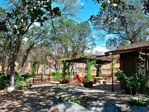 A covered outdoor seating area with tables and chairs, surrounded by potted plants and trees. - Quiet Cottage Rental for Two in Horse Country near Yosemite National Park Gateway, California (Catheys Valley)