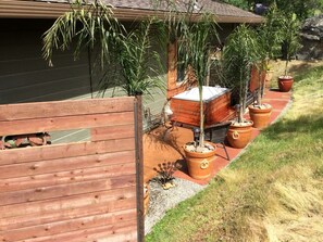 A wooden fence, potted plants, a patio area with a table and chairs, and a building with a sloped roof.
